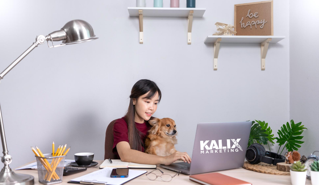 Young lady working remotely at her computer with a small dog on her lap